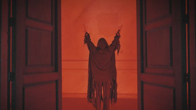 Sneaky robed person with arms up under a red light.